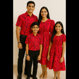 Family wearing red and black leaf print coordinated outfits – father in shirt, mother and daughter in dresses, and son in shirt