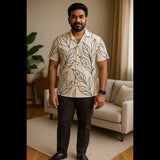 Man wearing beige leaf print shirt with black trousers, standing indoors in a modern living room.