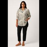 Plus-size woman wearing a beige oversized shirt with black leaf print and black ankle pants