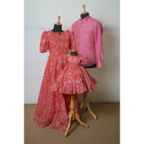 Coordinated pink floral family outfit featuring a puff-sleeve maxi gown for mom, rose chambray shirt for dad, and tiered sequin frock for baby girl.