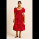 Indian woman wearing a red puff sleeve midi dress with bold black floral prints, styled for a chic festive look.