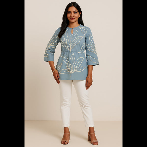Woman wearing a powder blue cotton top with off-white embroidered leaves, paired with white pants