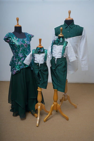 Emerald green family ethnic wear set with mom’s sequin blouse, dad’s white and green shirt, and matching kids' suspenders outfit.