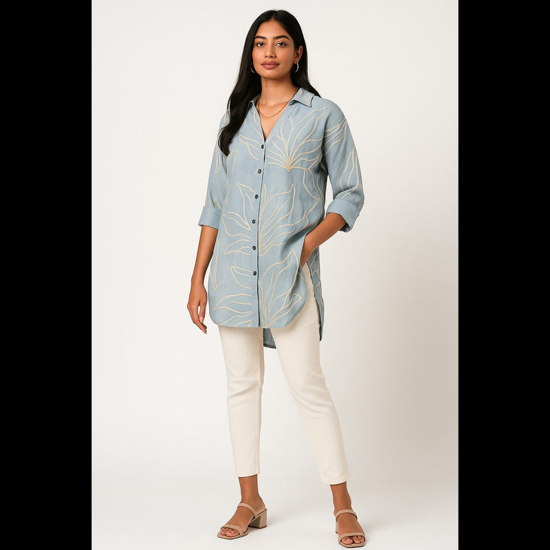Woman wearing sky blue long shirt with leaf embroidery and white slim-fit pants.