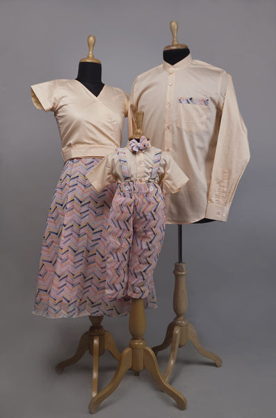 Pastel Chevron & Beige Family Outfit Set featuring mom's printed skirt set, dad's beige shirt with chevron pocket, and baby boy's chevron suspender set with bowtie — displayed on mannequins.