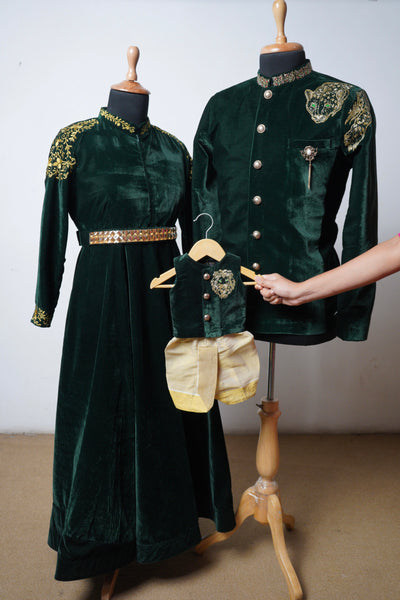 Family matching outfit in emerald green velvet featuring sherwani for dad, gown for mom, and dhoti set for baby boy