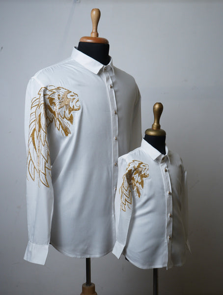 Father and son wearing matching white shirts with golden lion embroidery on shoulder and sleeve – festive family outfit.
