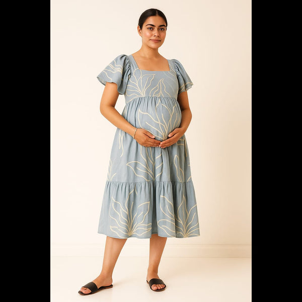 Pregnant woman in a sky blue maternity dress with white leaf print and flutter sleeves.