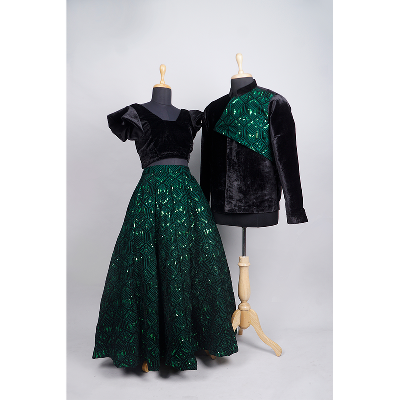 Emerald green velvet couple set with black velvet blouse and green sequin skirt for women, and matching velvet jacket with sequin detailing for men.