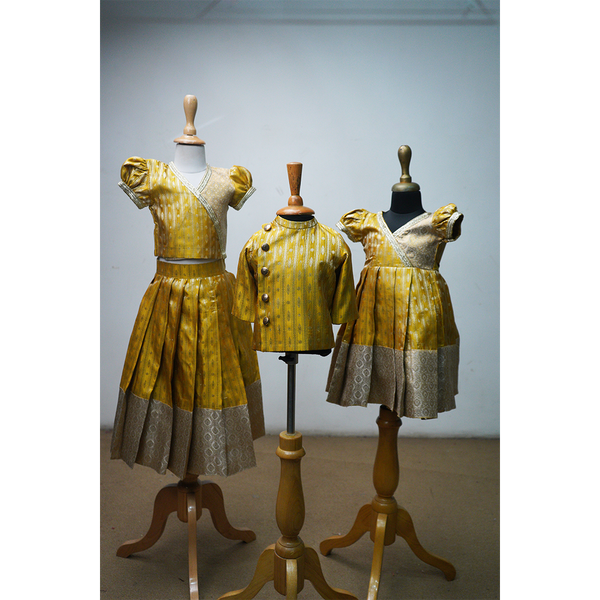 Golden brocade sibling combo featuring lehenga set, frock, and kurta displayed on mannequins.