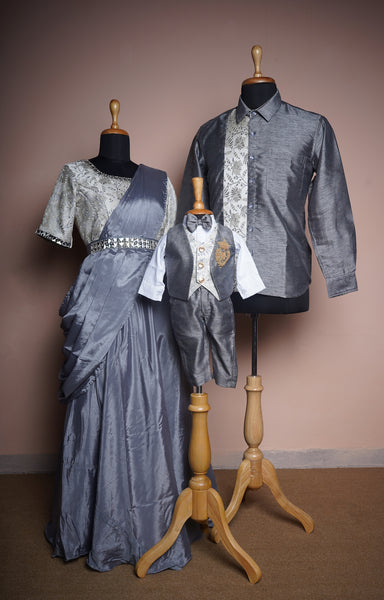 Steel grey family outfit set with a draped saree gown, brocade shirt for men, and a formal baby suit with embroidered crest and bow tie.